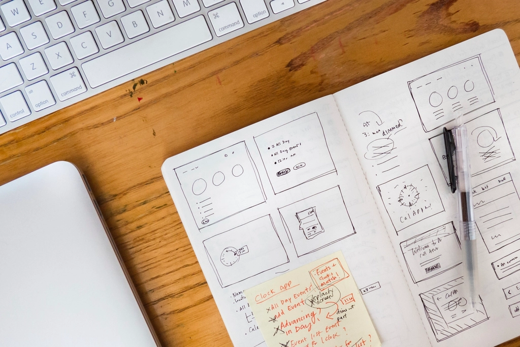 Notebook wireframes for a boutique website layout beside a keyboard and laptop